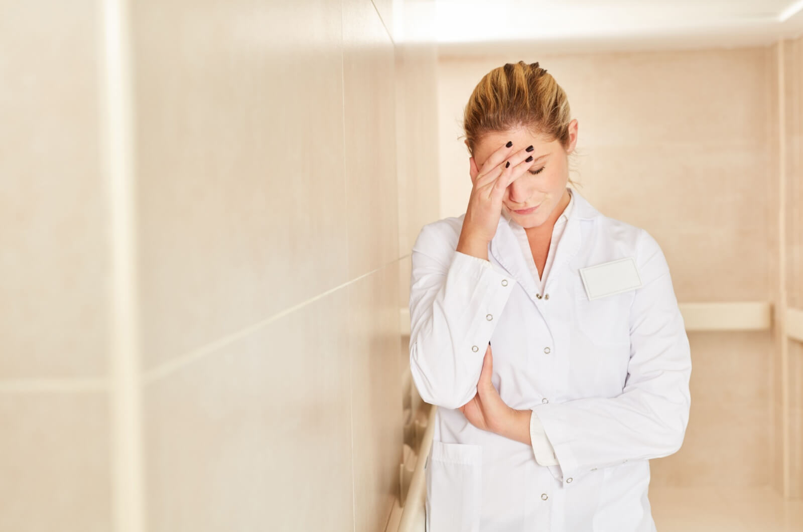 A caregiver in white coat touching their forehead from caregiver burnout.
