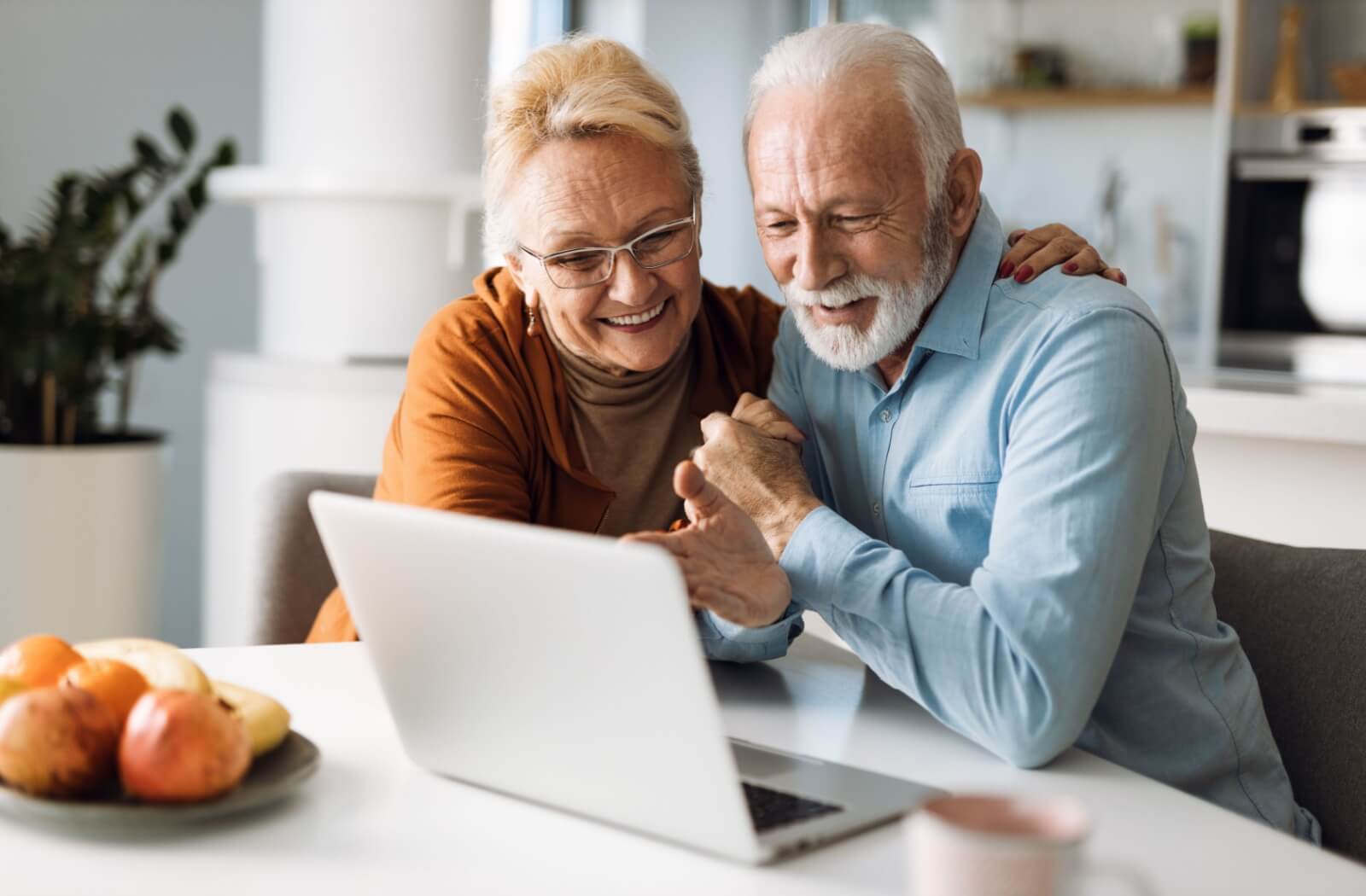 A senior couple at home explore senior living options on a laptop.