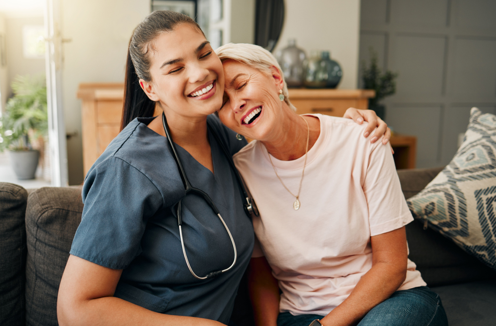 A caregiver hugging an older resident in senior living while they both laugh.