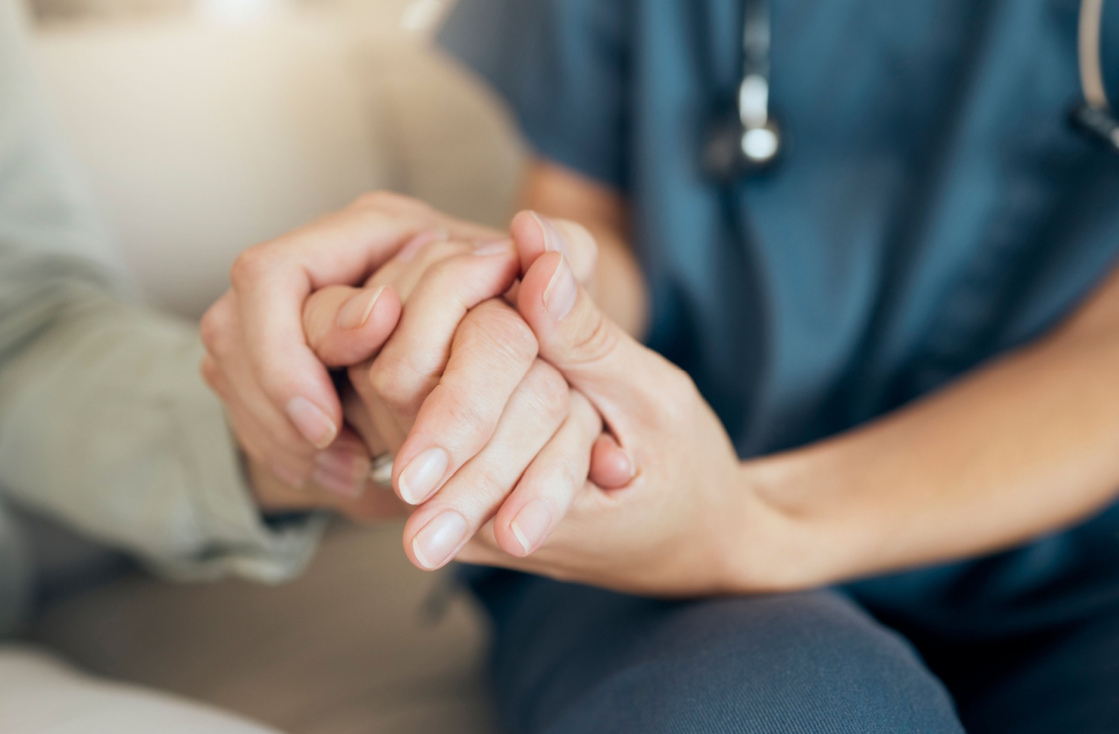 A close-up image of a caregiver holding the hand of an older resident in senior living.