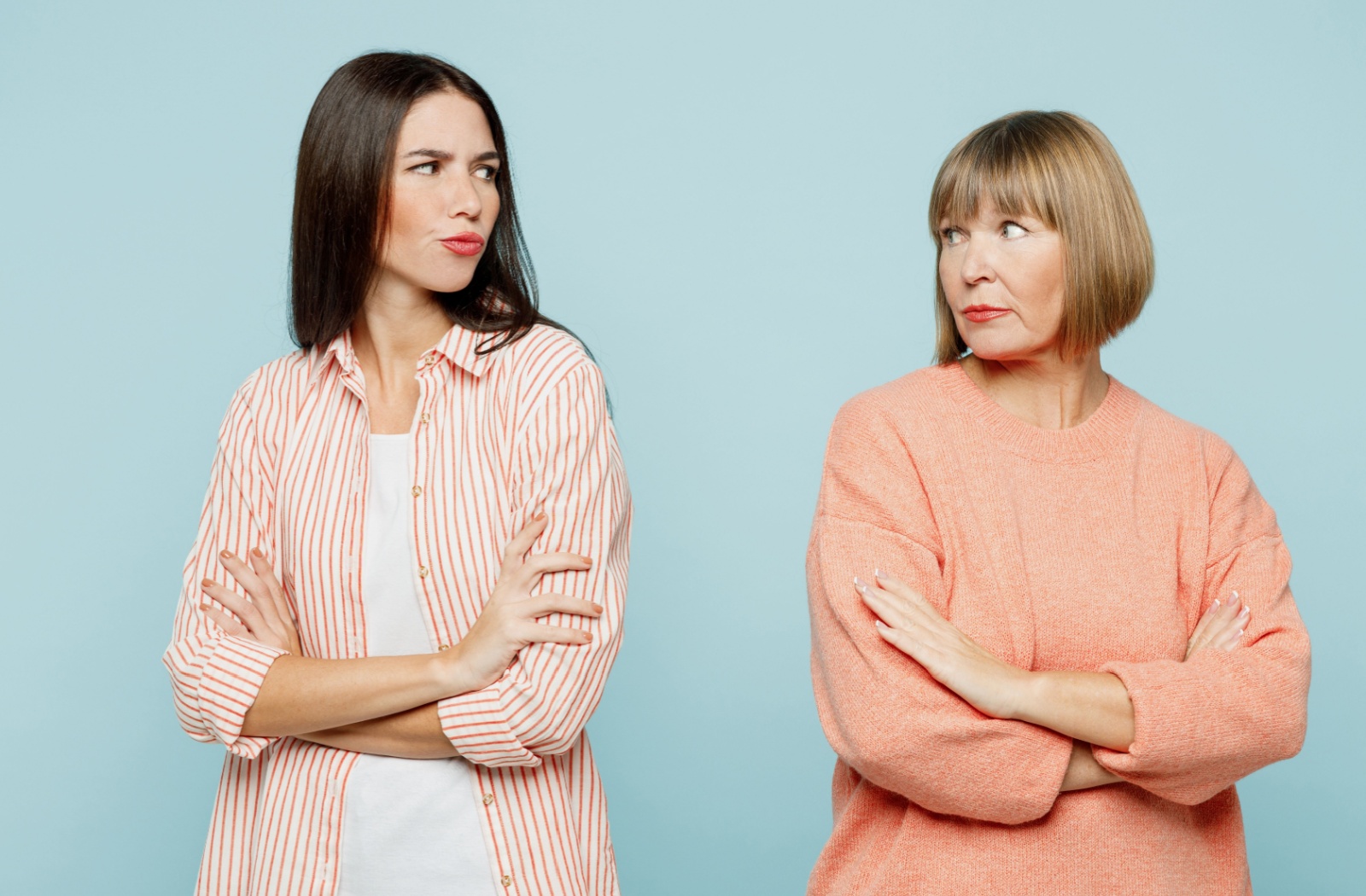 Against a pale blue backdrop, a disgruntled senior stands back to back with their adult child, caught in poor communication
