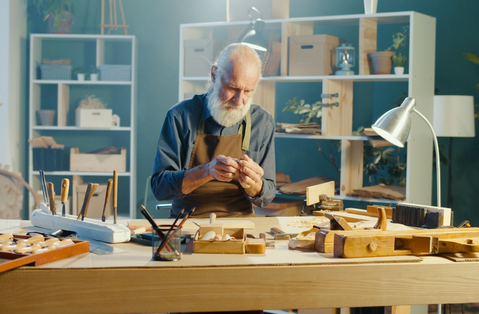 A senior sits in a woodworking workshop, using lots of light for detail work on a small wooden craft