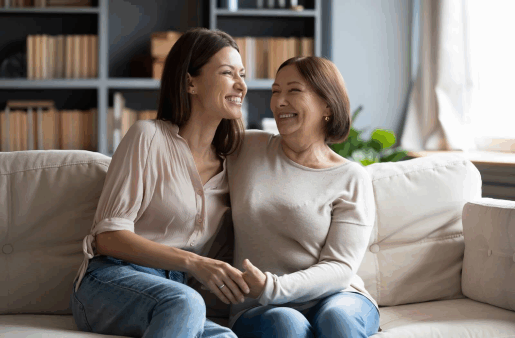 A senior and their adult child laugh together while embracing on the couch after solving a disagreement