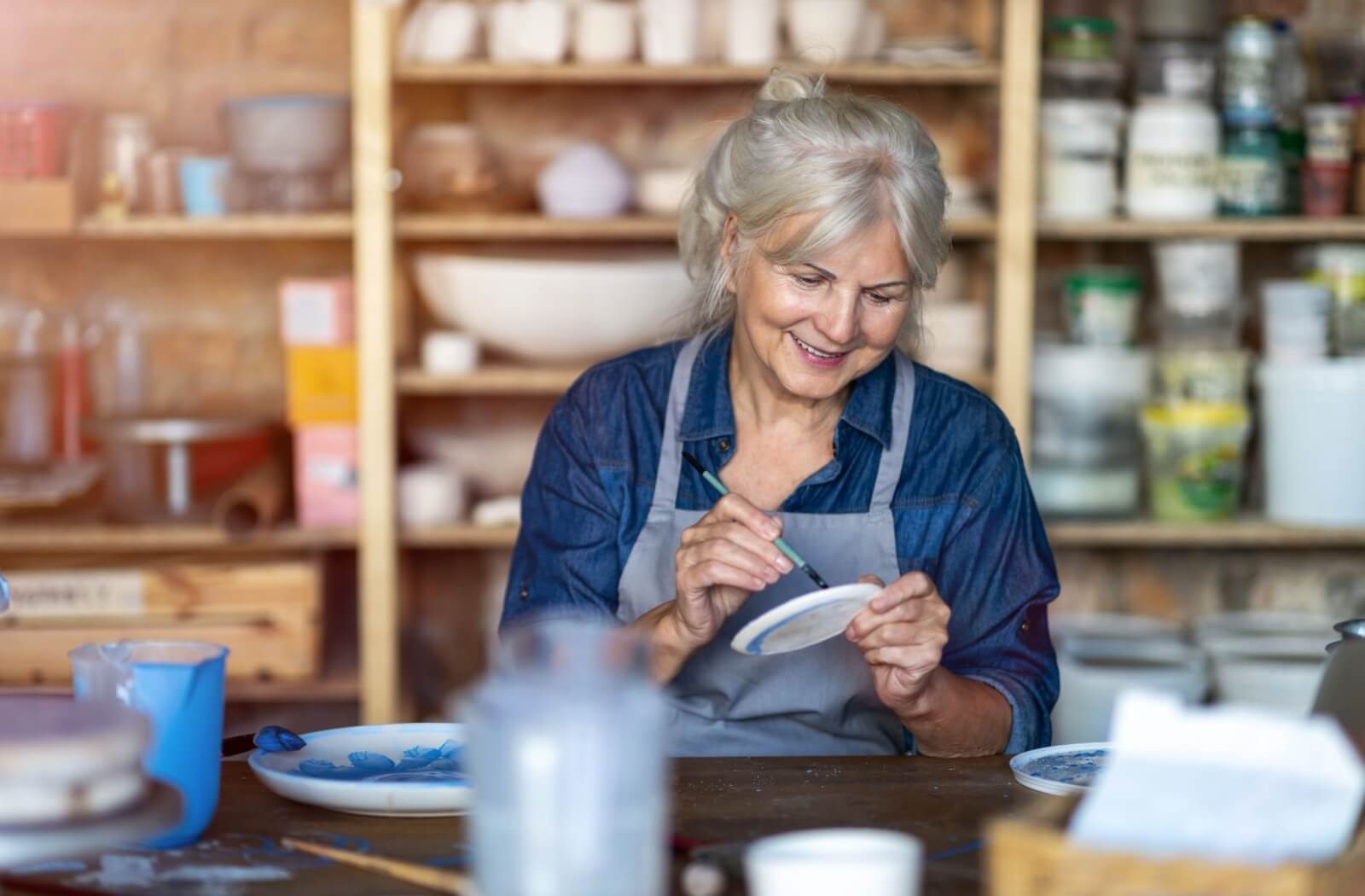 An older adult paints a piece of pottery that they made in a pottery studio.
