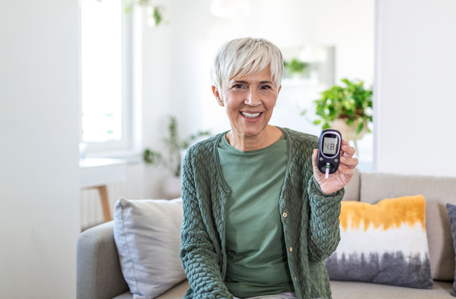A senior smiles while holding up a blood glucose monitor.