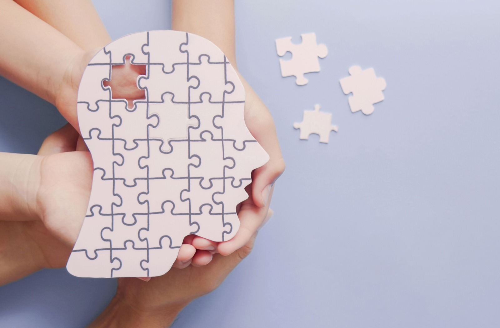 Hands holding up a puzzle in the shape of a head with a single piece missing, demonstrating symbolism of cognitive decline.
