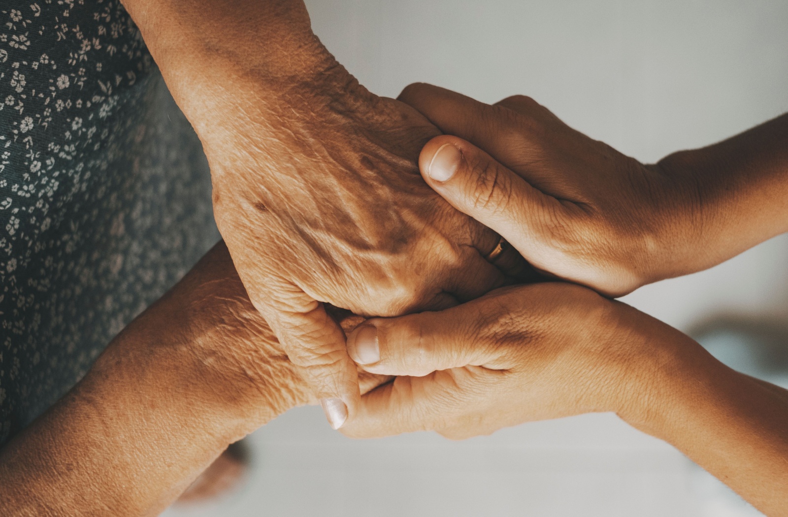 Close up of an adult child clasping hands with their senior parent.